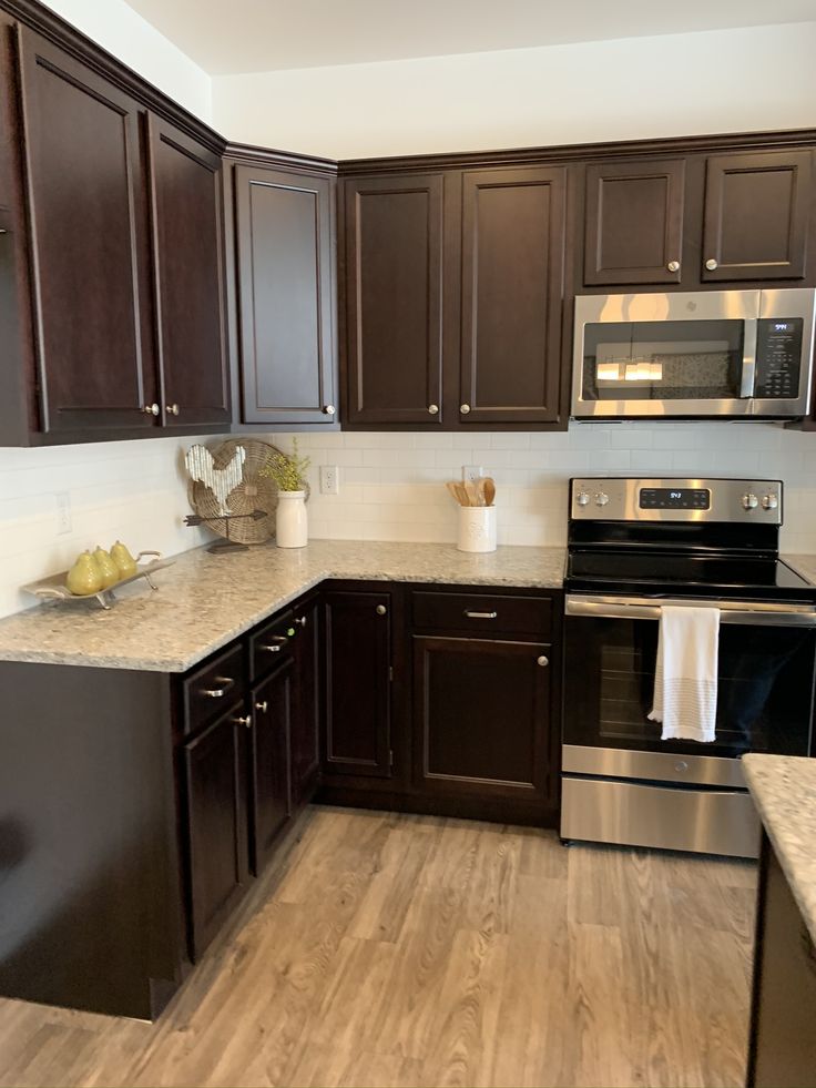 a kitchen with dark wood cabinets and stainless steel stove top oven, dishwasher and microwave