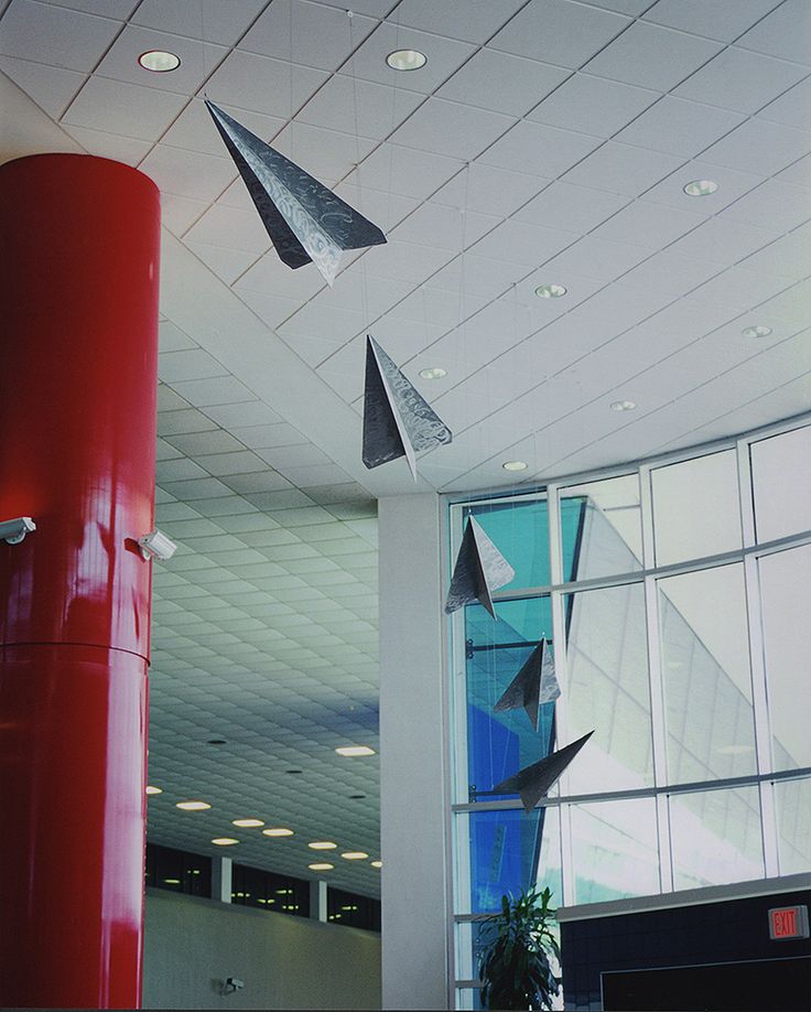 some birds are flying in the air near a red pillar and window at an airport