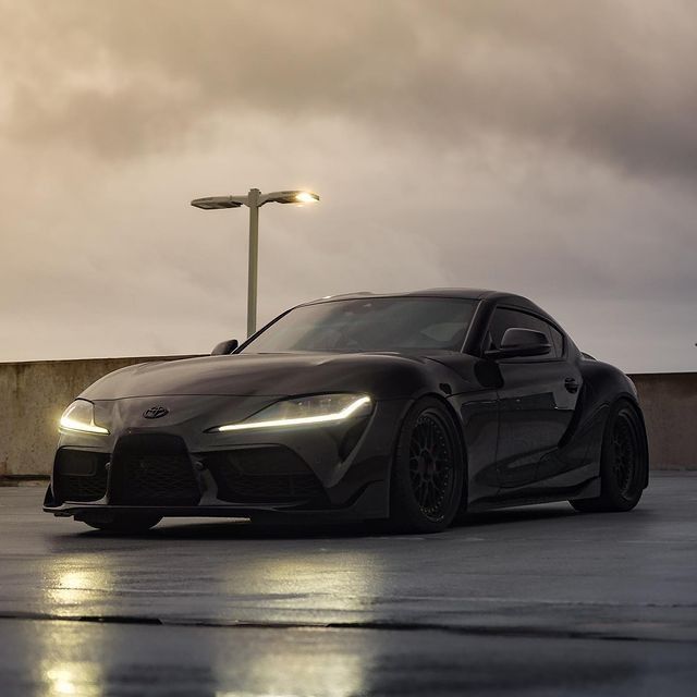 a black sports car is parked in the parking lot at night with its lights on