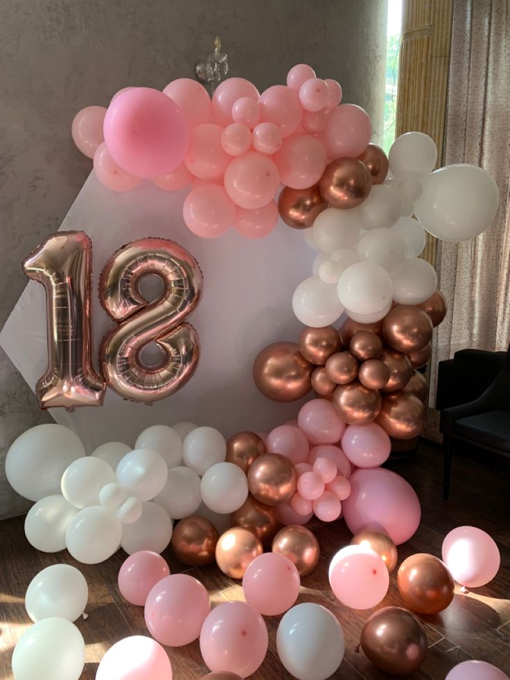 balloons and streamers are scattered around the number eighteen balloon arch for an elegant birthday party