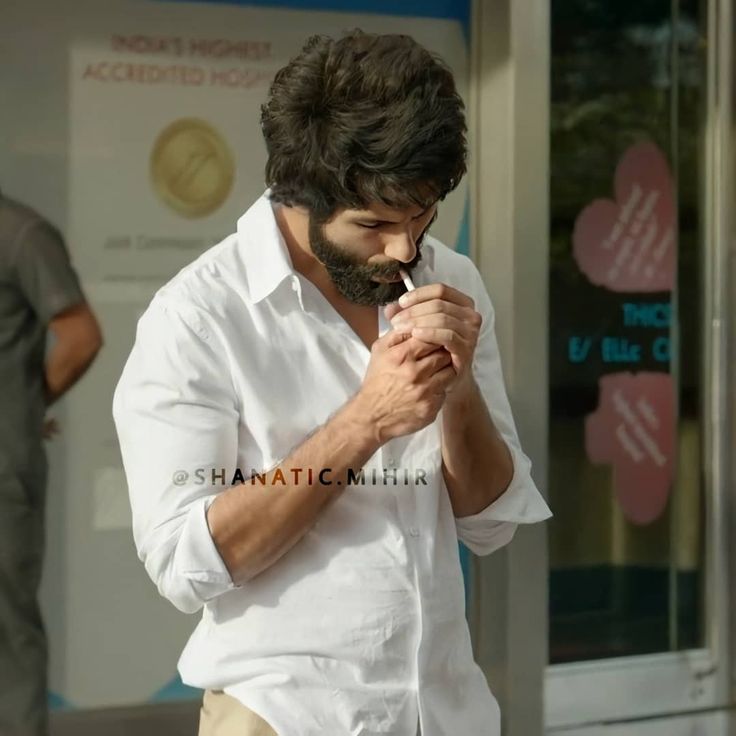 a man standing in front of a building looking at his cell phone while wearing a white shirt and khaki pants