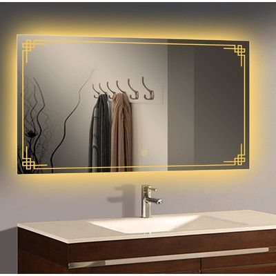 a bathroom vanity with a lighted mirror above it and clothes hanging on the rack below