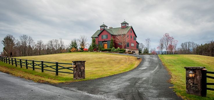 a large red house sitting on the side of a lush green field next to a road