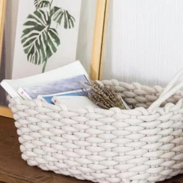 a white basket sitting on top of a wooden table next to a framed photo and plant