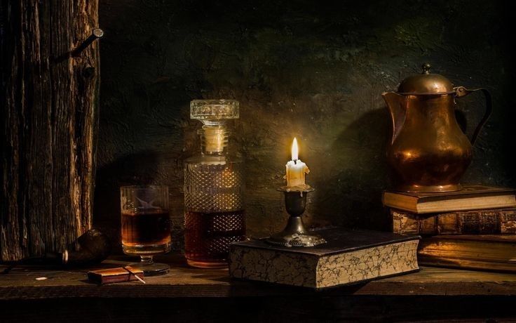 a table topped with books and a lit candle next to a book case on top of a wooden shelf