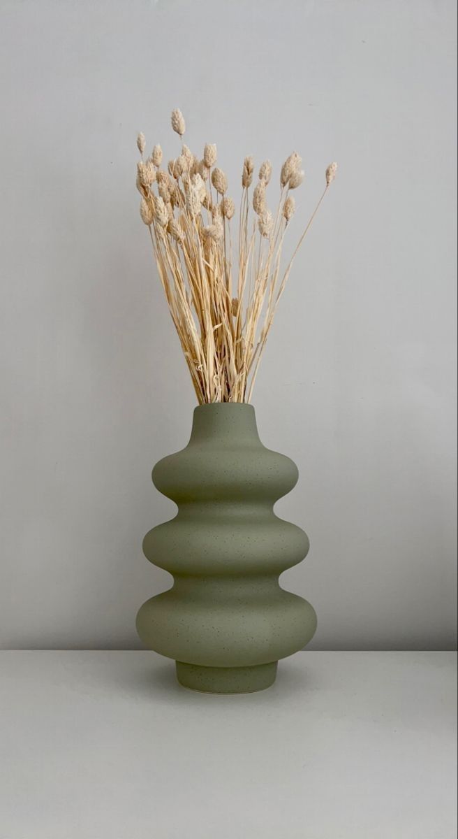 a green vase with some dry grass in it