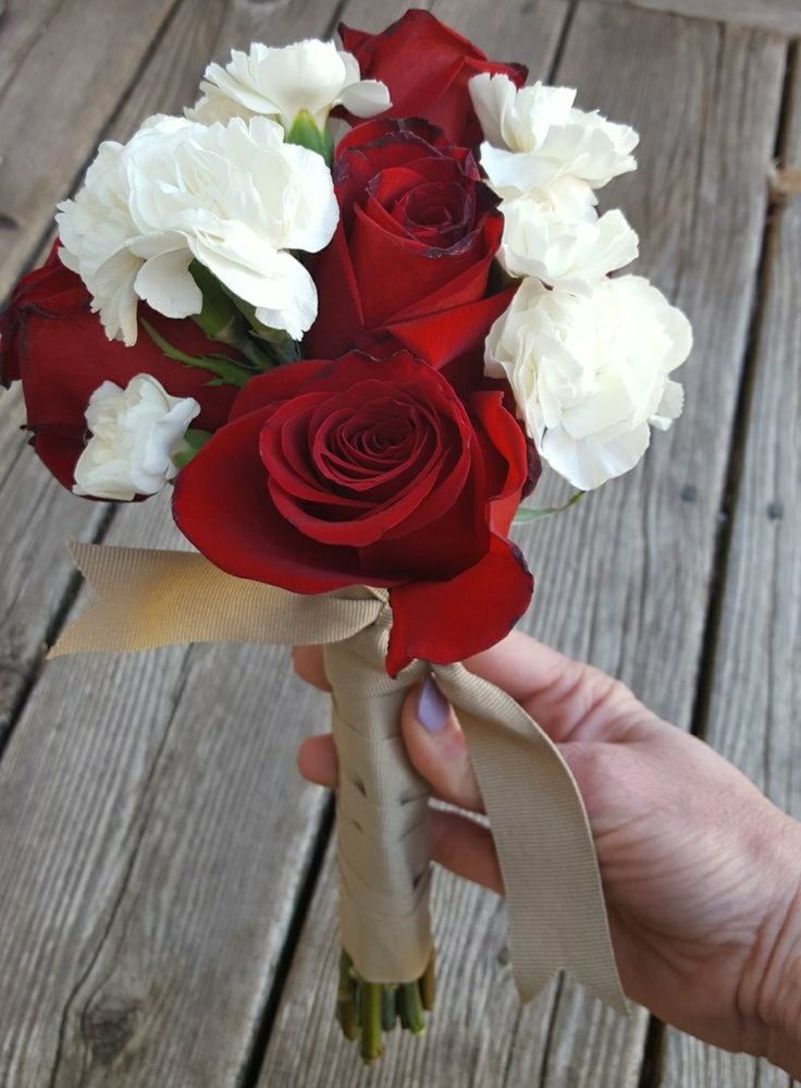 a bouquet of red and white flowers is being held by someone's hand on a wooden deck