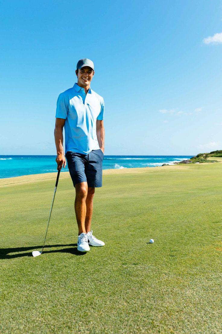 a man standing on top of a lush green field next to a golf ball near the ocean