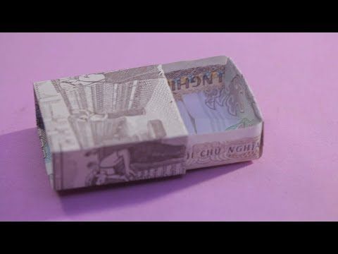 an origami money box sitting on top of a pink surface with purple background