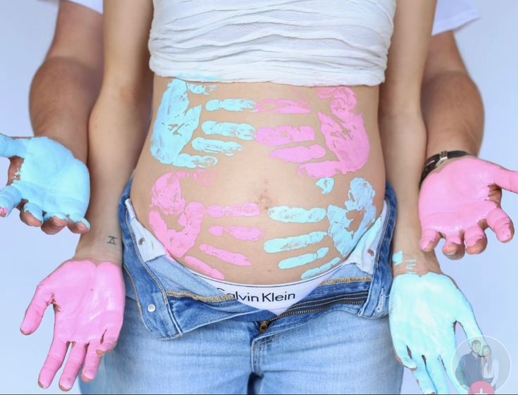 a pregnant woman with painted hands on her stomach and belly in blue, pink and white colors