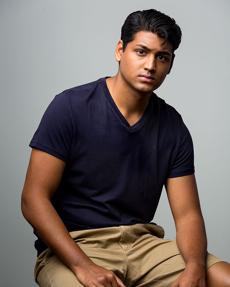 a young man sitting on top of a wooden chair wearing a black shirt and khaki pants