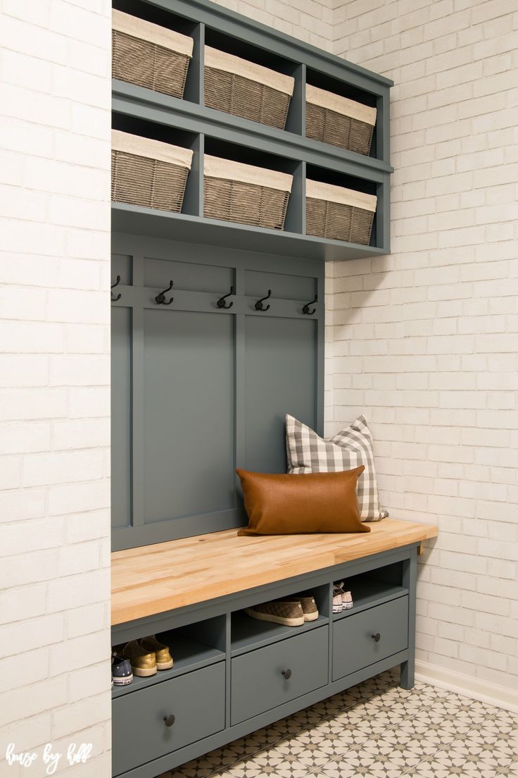 a bench with some baskets on it in front of a white brick wall and floor