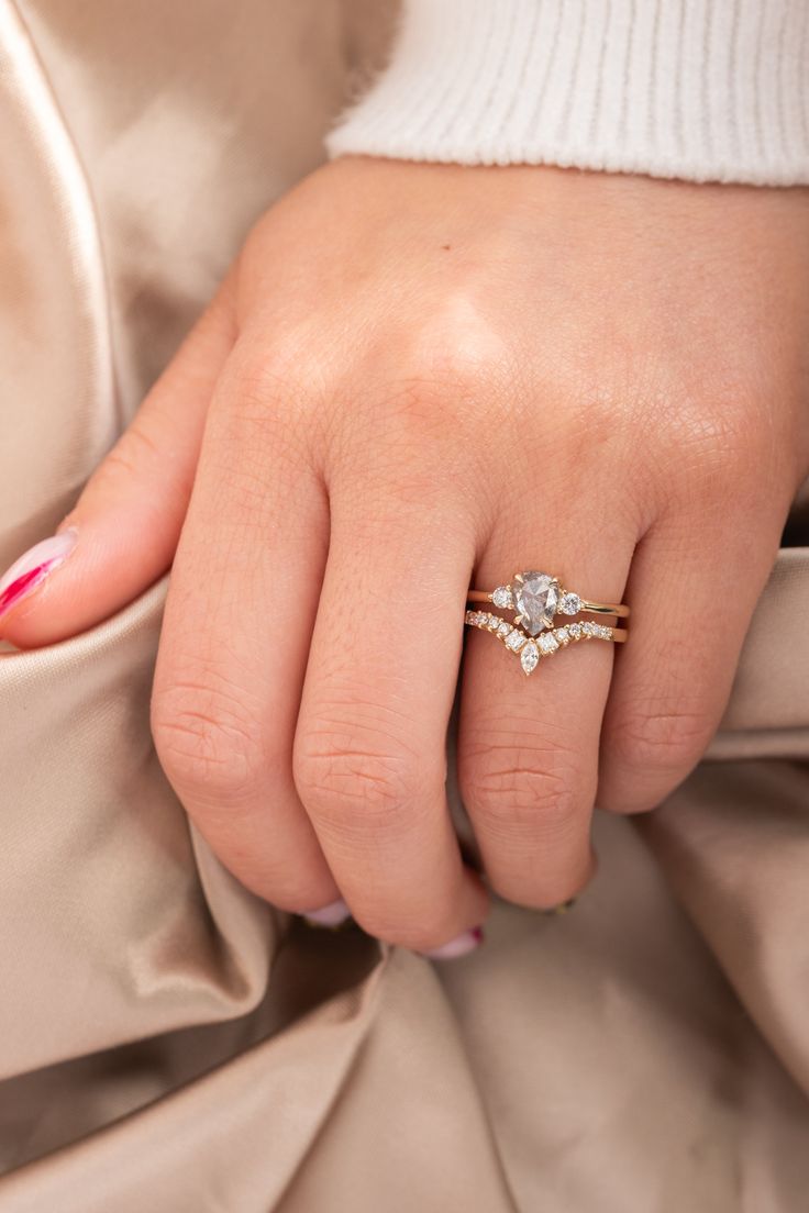 a woman's hand wearing a gold ring with two diamonds on it and a pink manicure