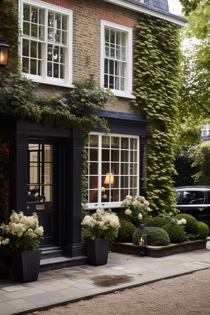 a building with many windows and plants on the front porch, along with a car parked outside