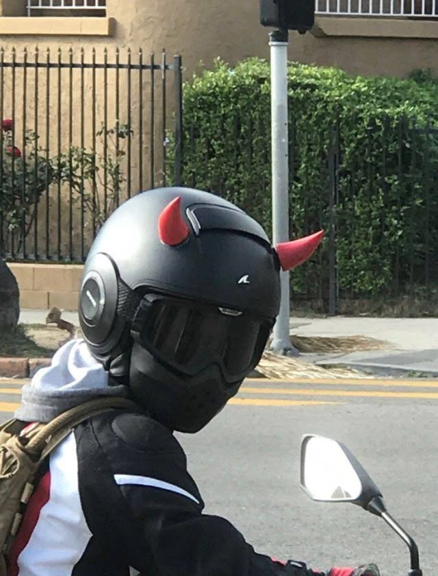 a person on a motorcycle wearing a helmet and bull horns is riding down the street