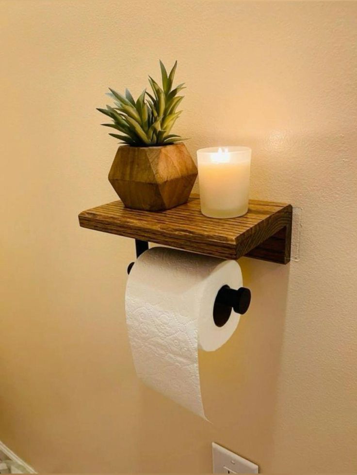 a toilet paper holder with a candle on it and a potted pineapple in the corner