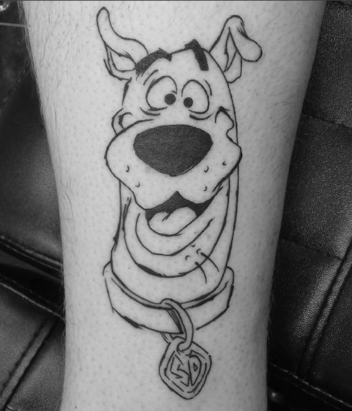 a black and white photo of a cartoon character tattoo on the leg, with a dog tag attached to it