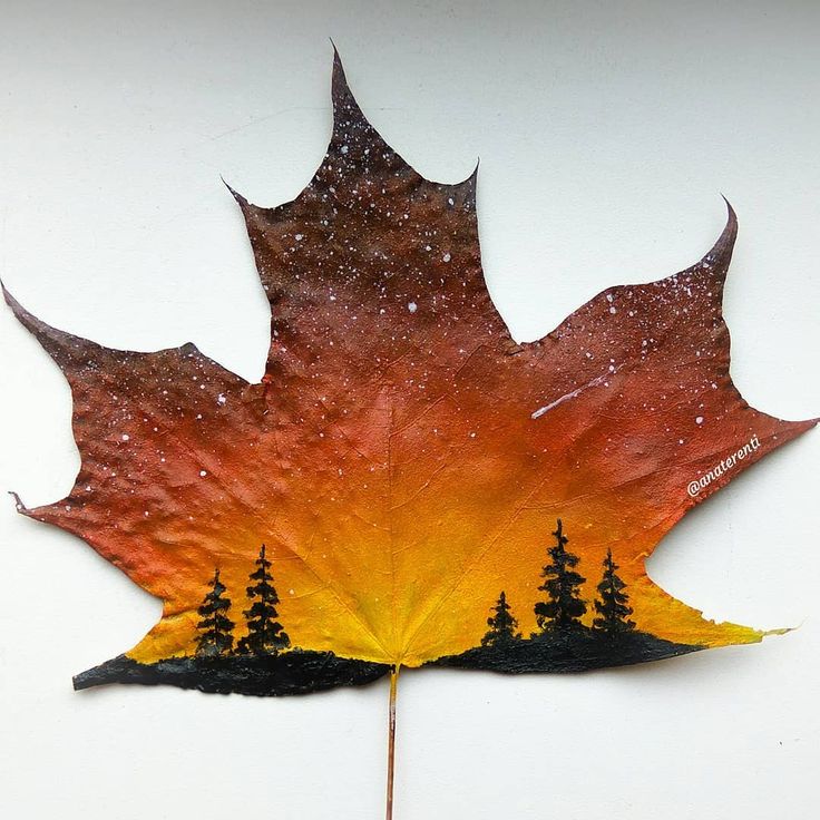 a leaf that has been painted to look like it is falling from the sky with trees on it