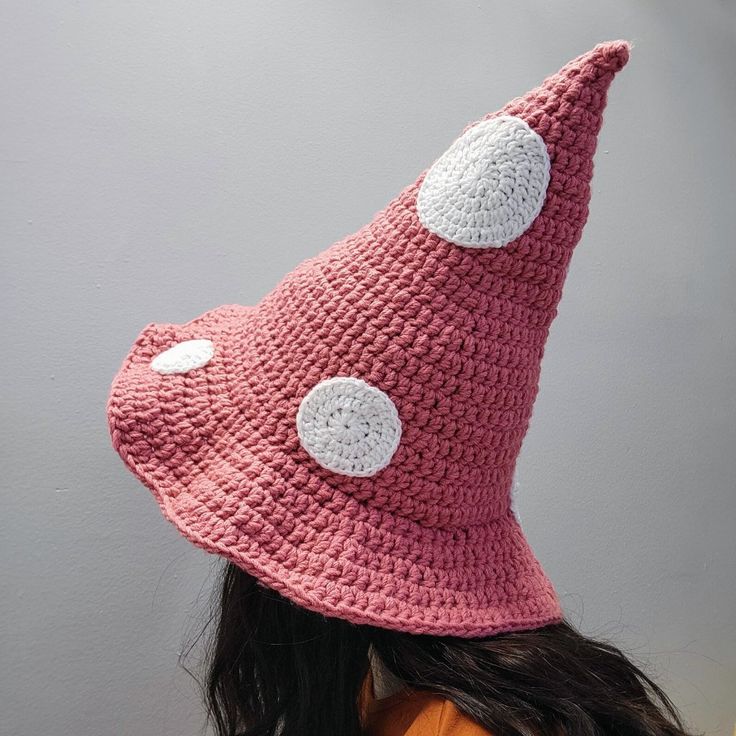 a woman wearing a pink crocheted hat with white polka dots on the side