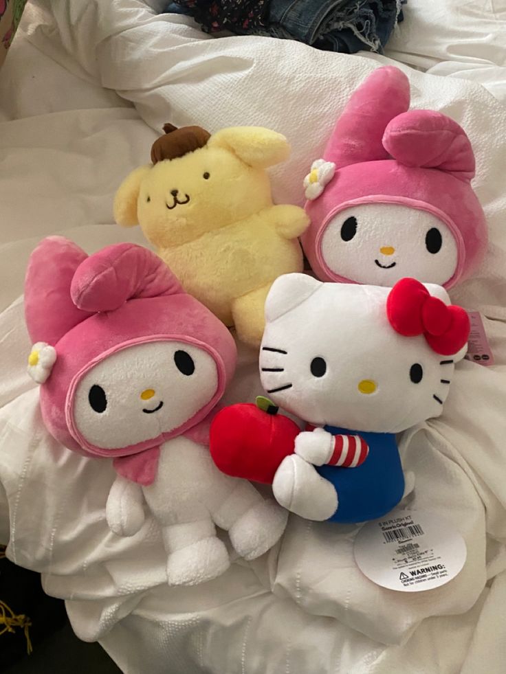 three hello kitty stuffed animals on a bed