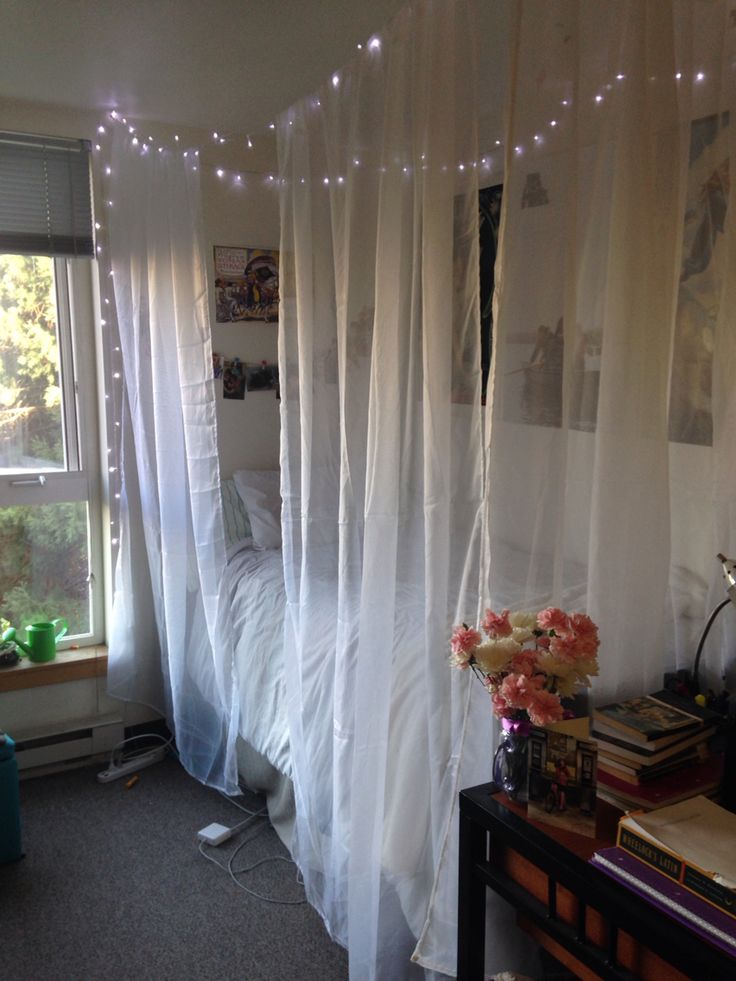 a bedroom with sheer curtains and flowers on the bed, next to a window that is lit by fairy lights