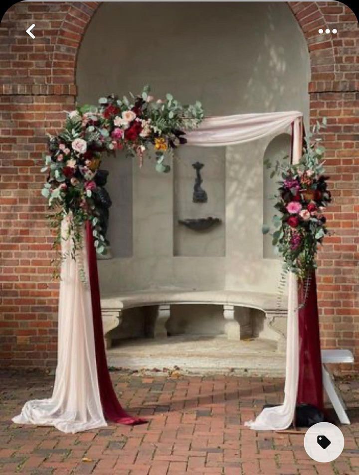 an arch decorated with flowers and greenery in front of a brick wall at a wedding