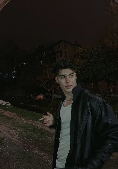 a young man standing in front of a building at night with his hand on his hip