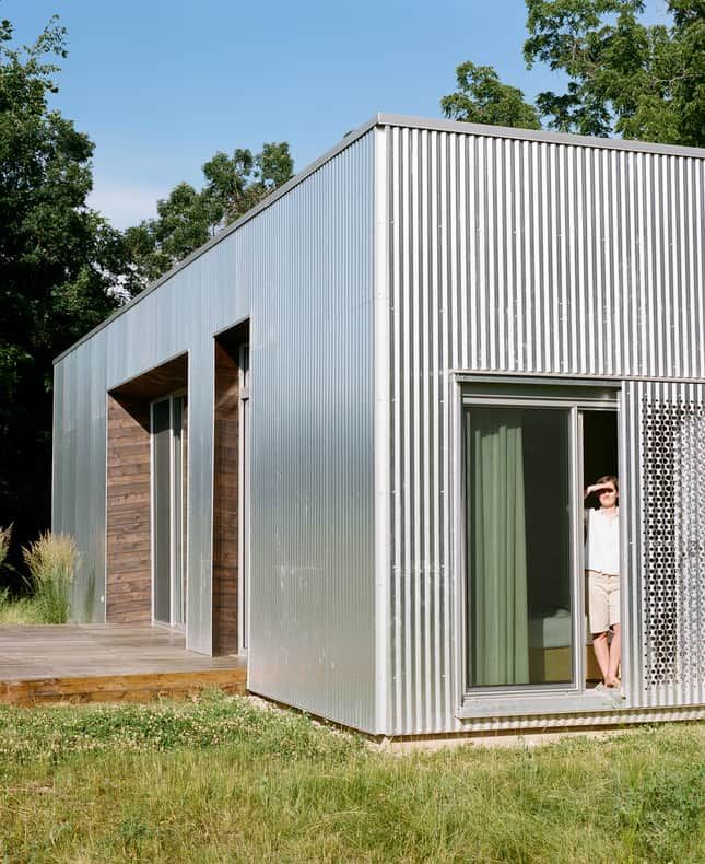 a small metal building sitting on top of a lush green field next to a forest