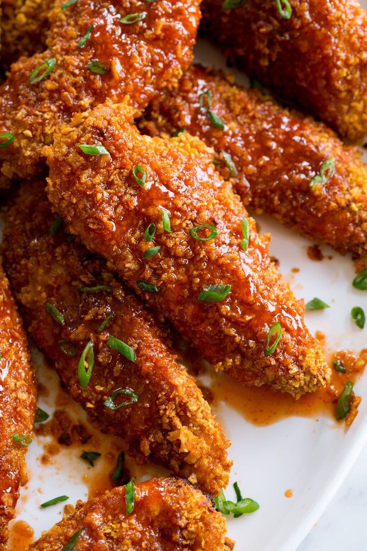 fried chicken wings covered in sauce and parsley on a white plate with green garnish