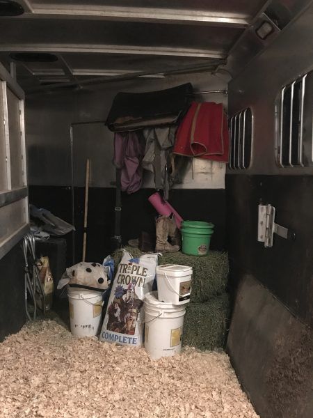 the inside of a horse trailer with hay and buckets on the ground next to it