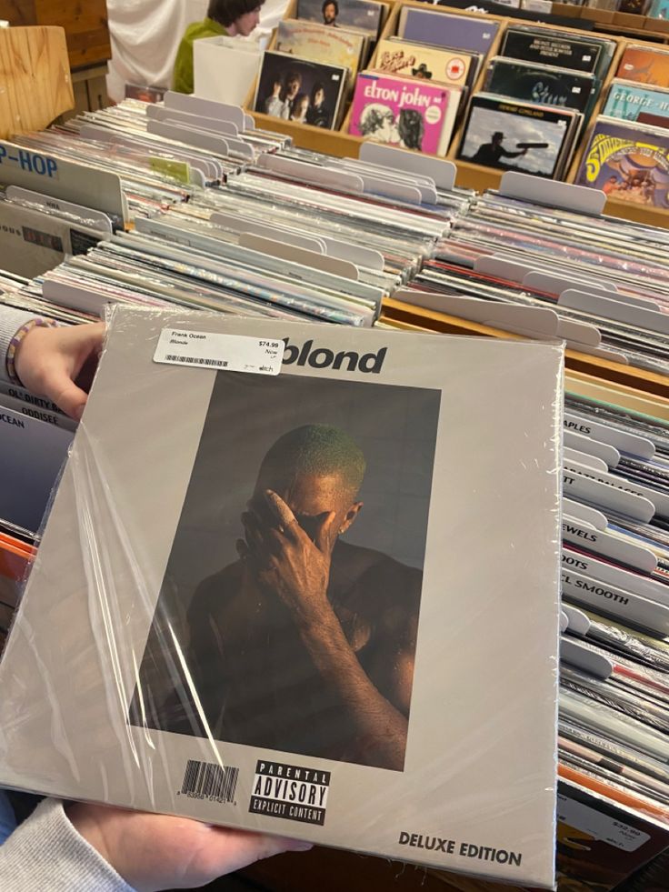 a person holding up a cd case in front of a table full of record albums