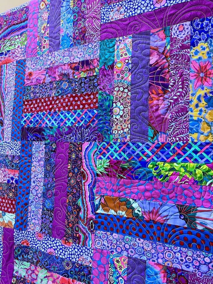 a colorful quilt is hanging up on the side of a building with lots of different colors and patterns