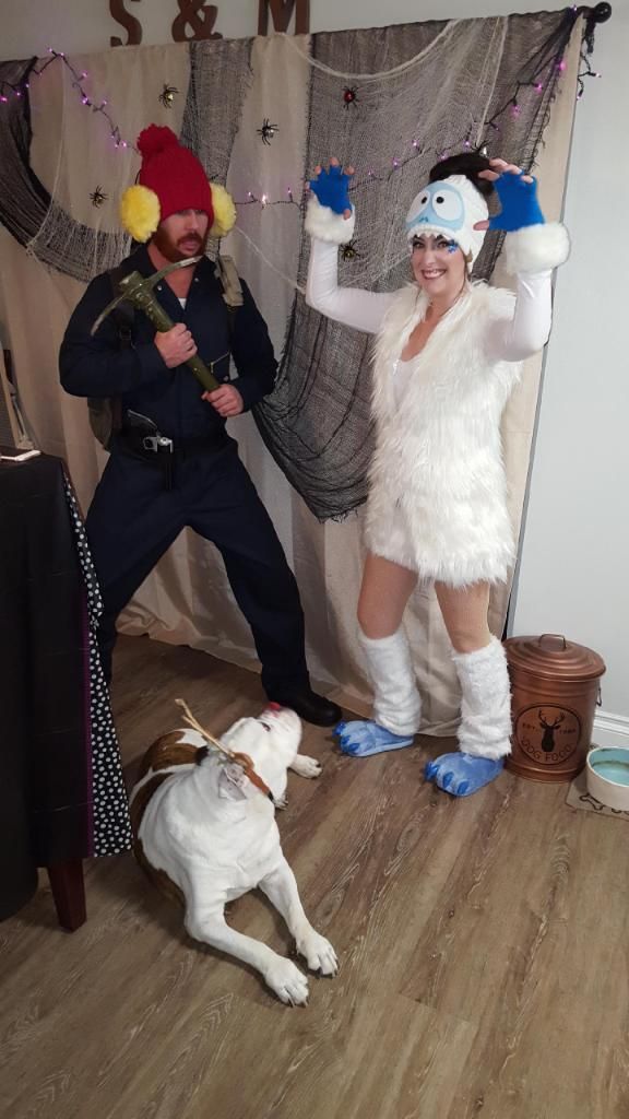 two people dressed in costumes standing next to a dog on the floor and one person holding something