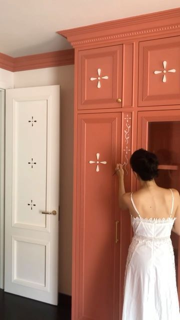 a woman in a white dress standing next to a red cabinet and looking at the door