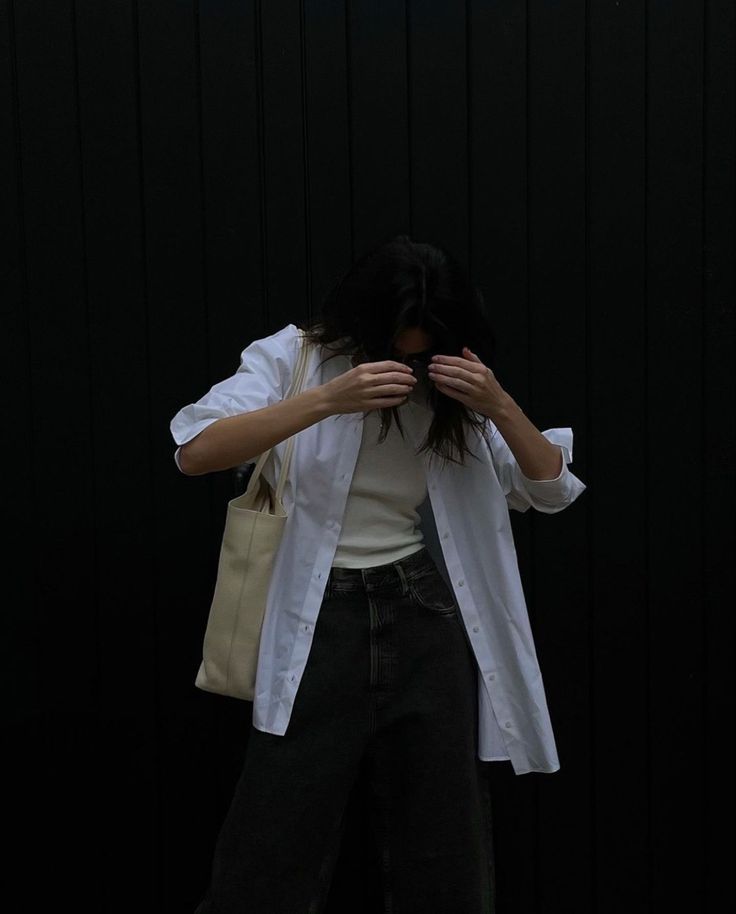 a woman standing in front of a black wall covering her eyes