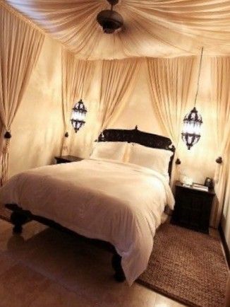 a bed with white sheets and pillows in a room that has curtains on the ceiling