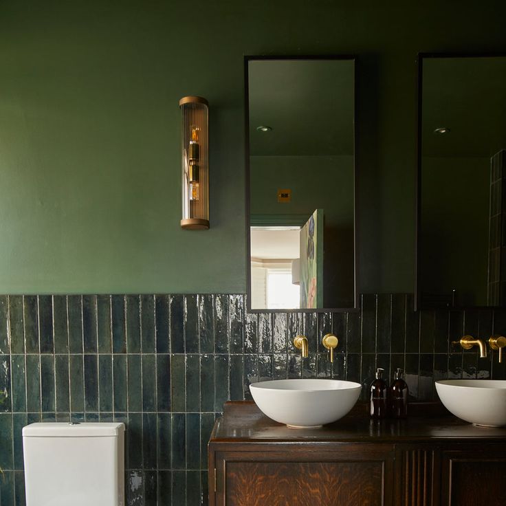 a bathroom with two sinks and a toilet next to a mirror on a green wall