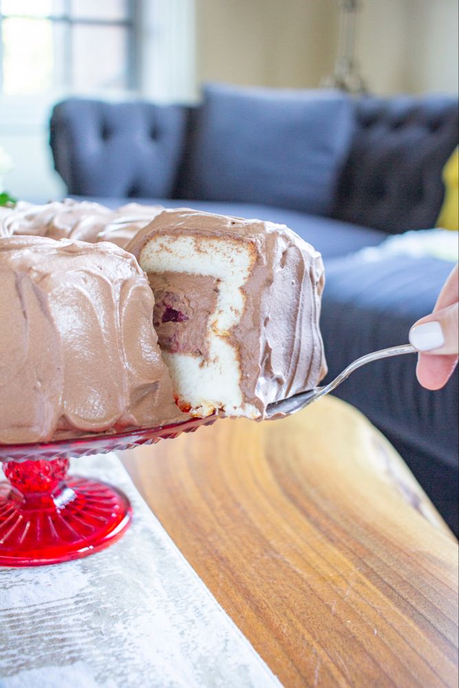 a person is holding a piece of cake with chocolate frosting on it and the rest of the cake has been cut