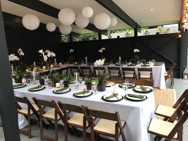 a table set up with white flowers and greenery for an outdoor dinner or party