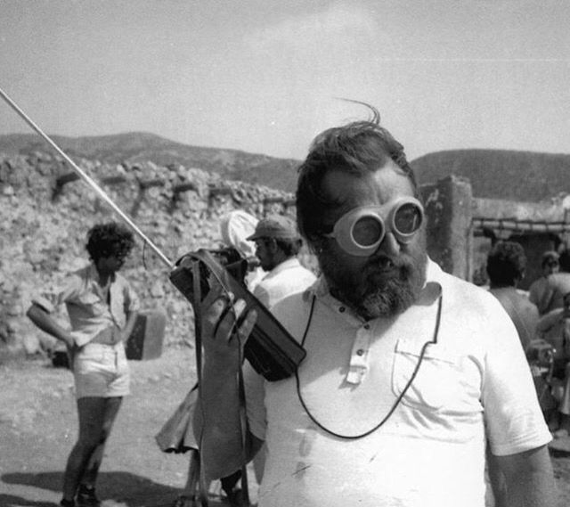 a man with goggles and a beard is standing in front of a group of people