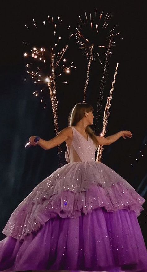 a woman in a purple dress with fireworks behind her