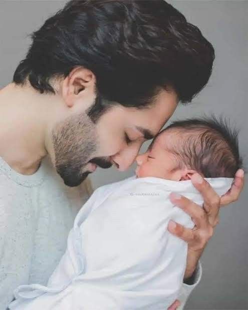 a man holding a baby in his arms and kissing it's face next to another man