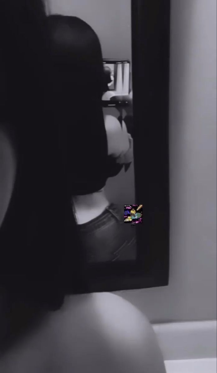 a woman taking a selfie in front of a mirror with the reflection of her shirtless torso