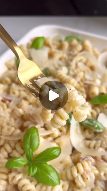 pasta with mushrooms and basil being held up by a fork in a white dish on top of a table