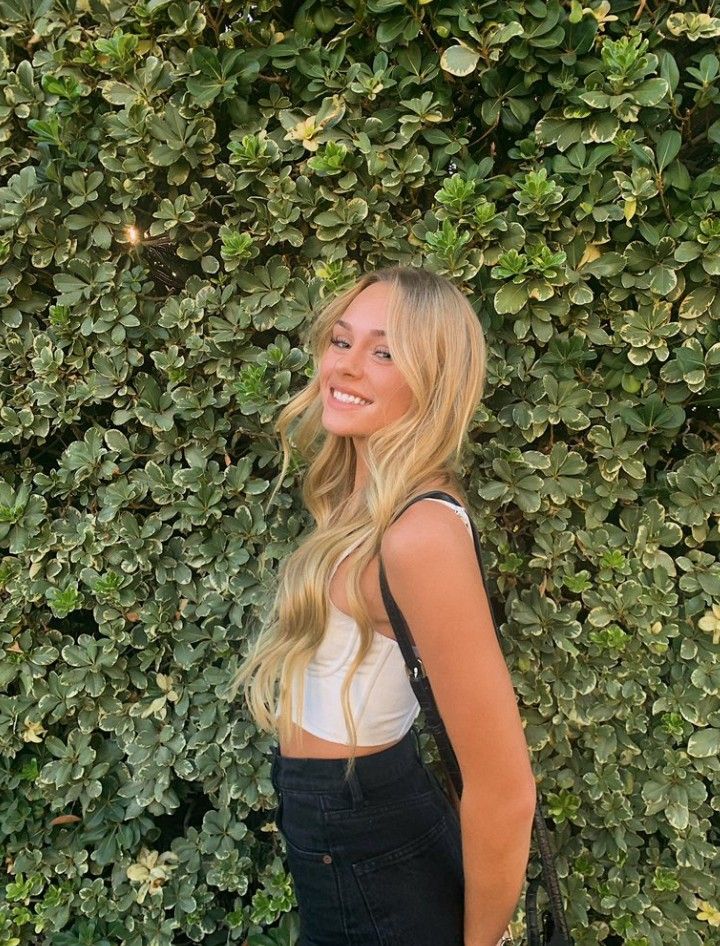 a beautiful young blonde woman standing in front of a hedge