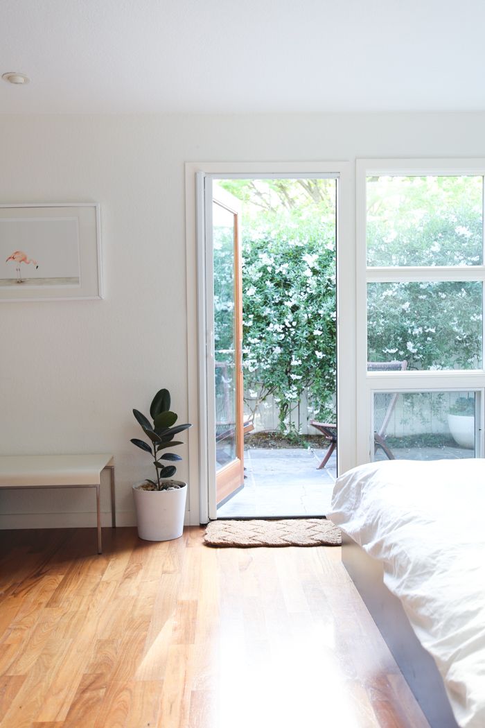 a bed sitting in a bedroom next to an open glass door with a plant on top of it