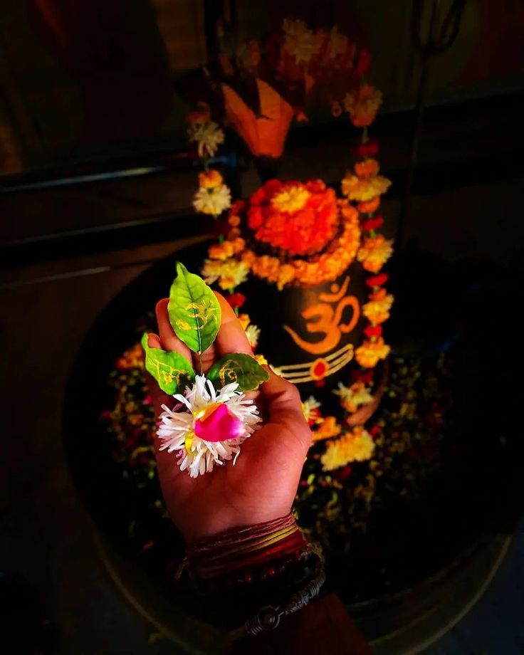 a hand holding a flower in front of a cake with flowers and leaves on it