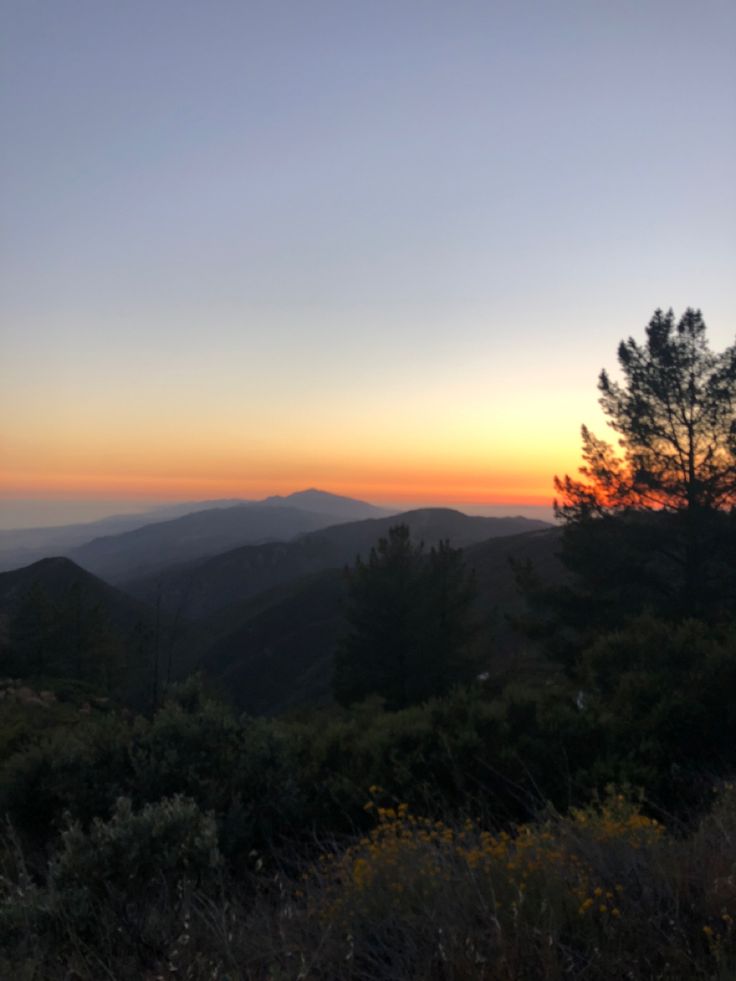 the sun is setting in the mountains with trees and bushes on either side of it