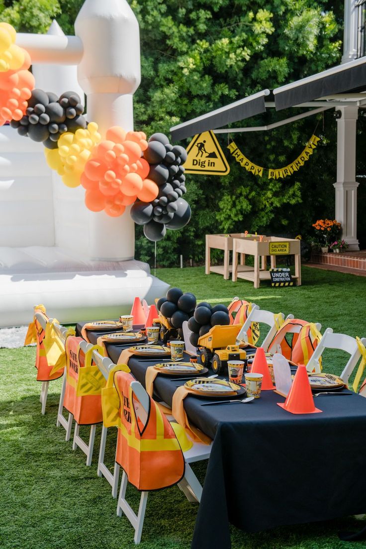 an outdoor party with black and orange decorations, balloons and table cloths on the grass