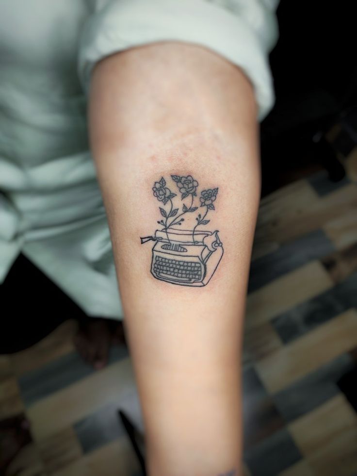 a woman's arm with a tattoo that has a typewriter and flowers on it